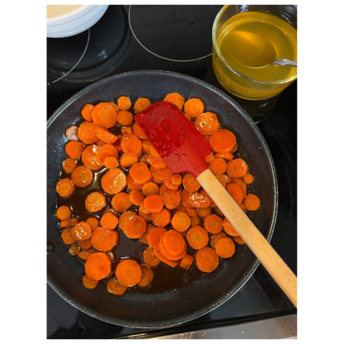 frying pan of cut up carrots with a spatula and bowl of reserved carrot water