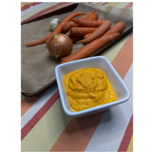 white bowl puréed carrots in forefront of photo with carrots and onions on baking sheet in the background